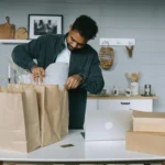 como-aumentar-as-vendas homem com sacolas e caixas e notebook aberto para vendas online
