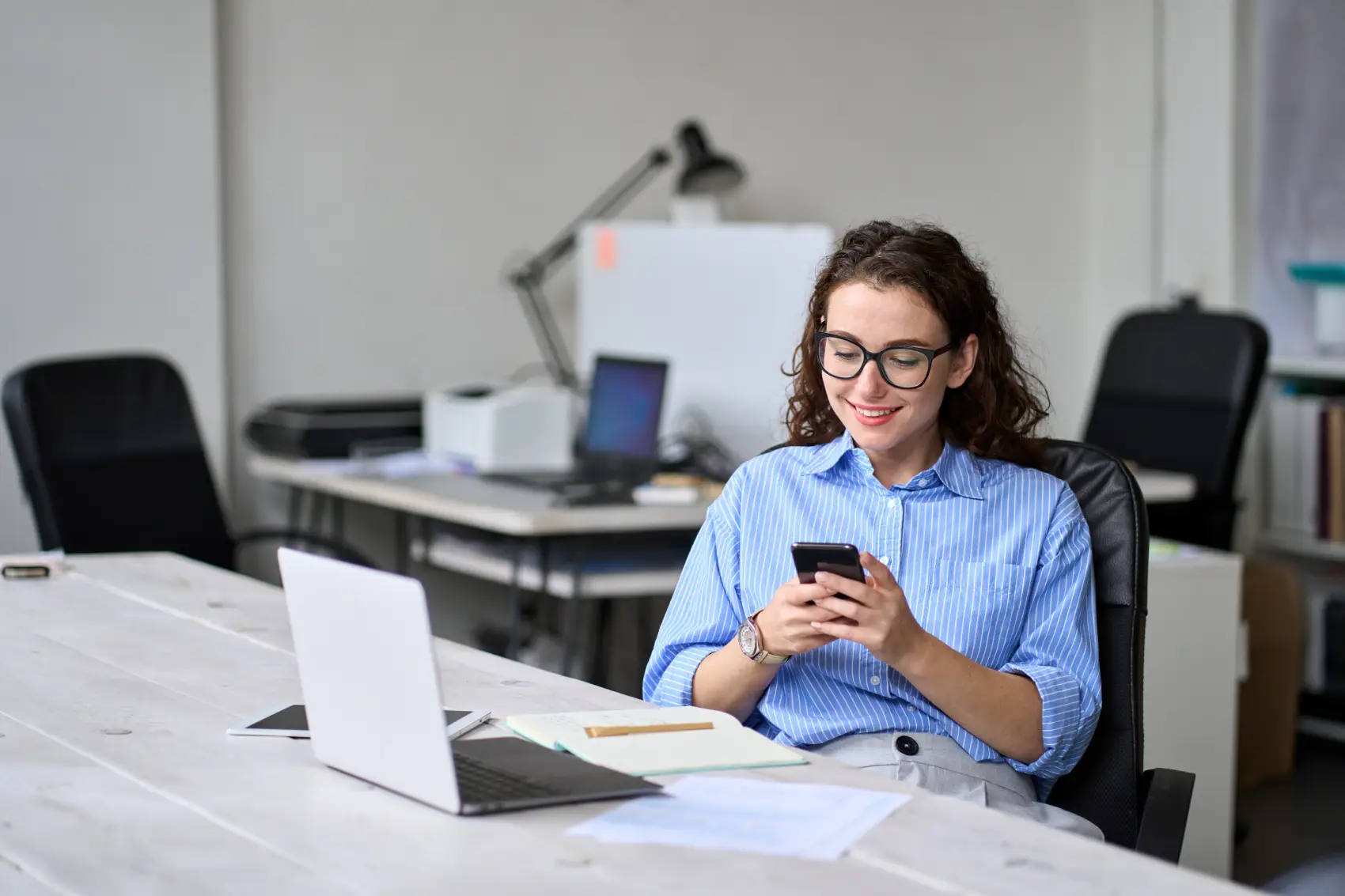 conta pj pagbank​ - mulher caucasiana sentada em frente ao notebook na mesa com celular na mesa
