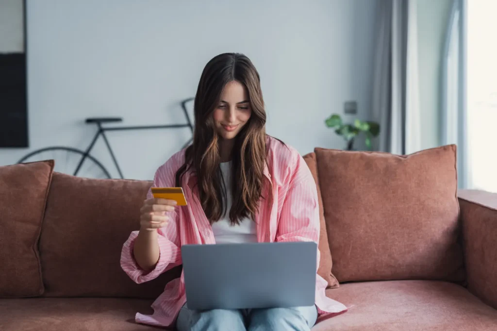 cuidados-e-golpes-com-cartao Cliente jovem sorridente da loja de internet satisfeita faz a compra e gasta dinheiro do cartão de crédito através do aplicativo para laptop