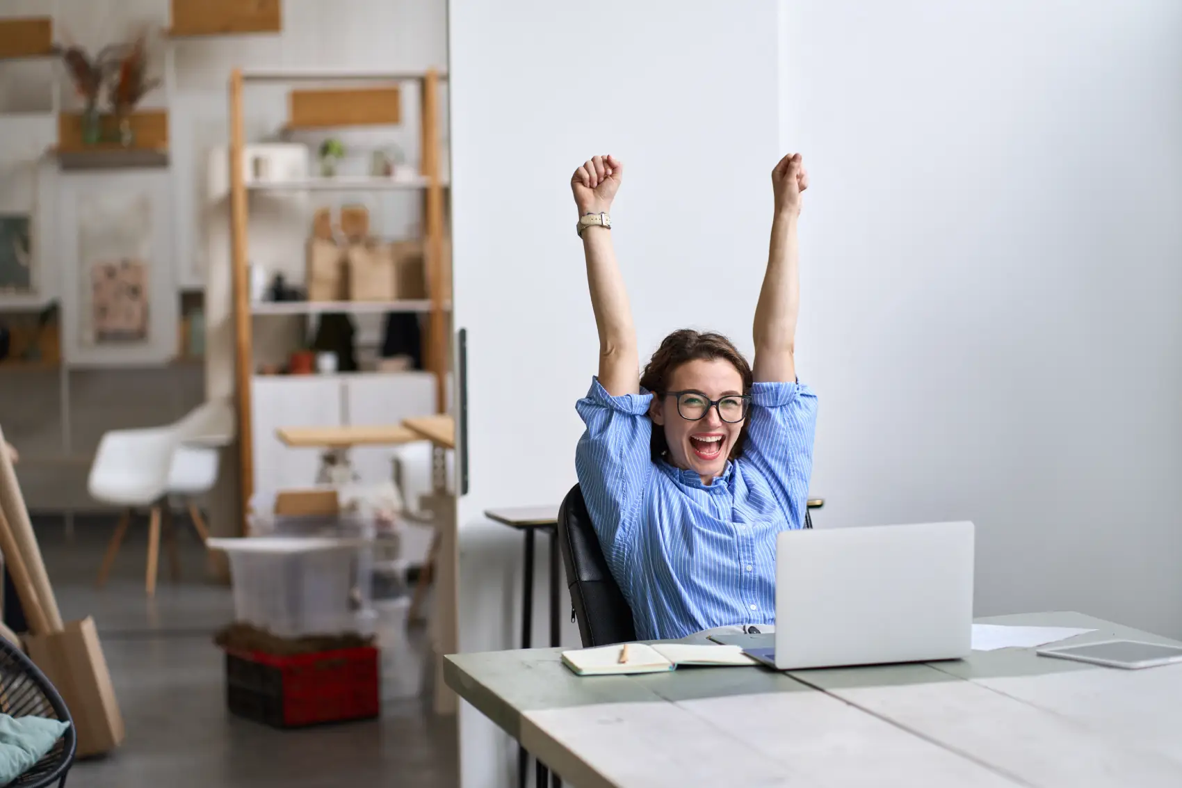 o que é abono salarial​ - mulher branca sentada em mesa em frente ao notebook com braços para cima, comemorando feliz
