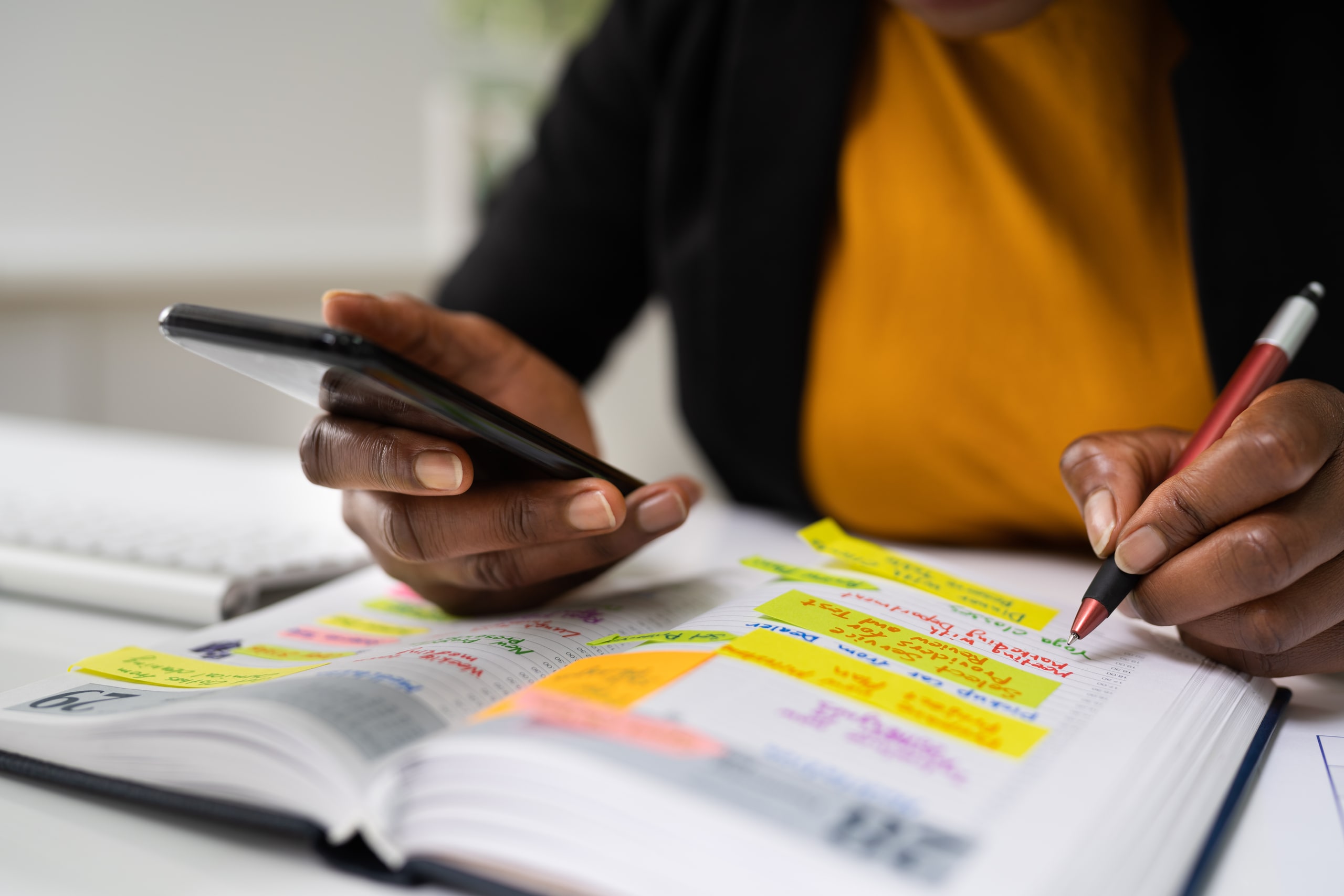 mulher fazendo anotações em planner com celular na mão