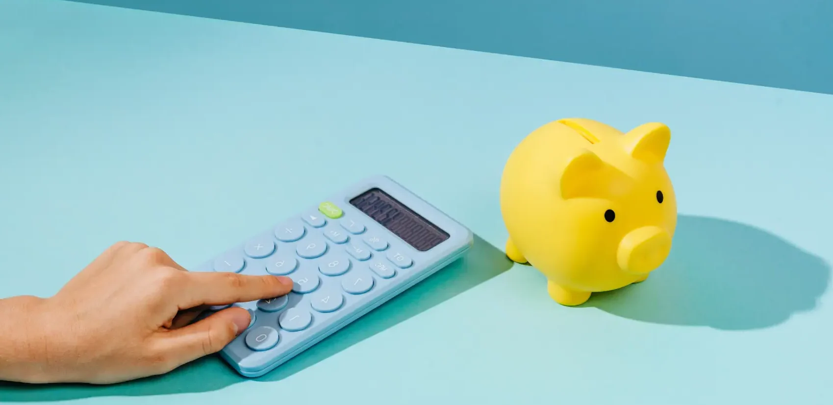 reserva de emergência - mão apertando calculadora azul em bancada com porquinho amarelo