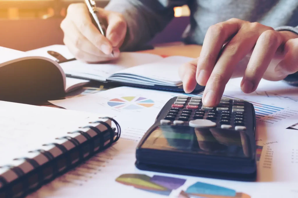 o que é precificação - mão masculina usando calculadora com gráficos na mesa
