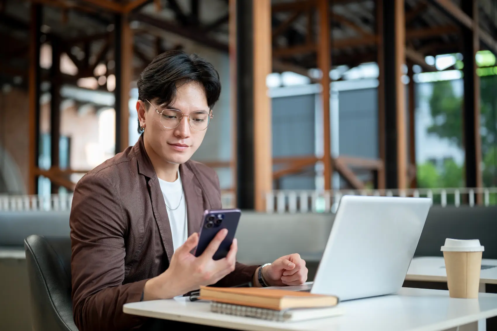 conta PJ - homem asiático sentado em café, em frente ao notebook, olha seu celular
