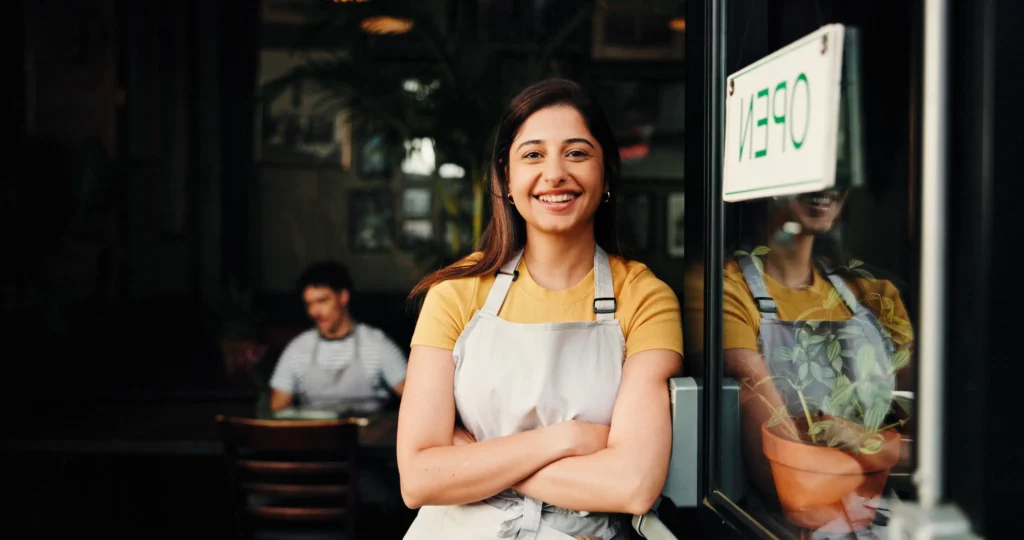 vantagens de ser mei - proprietária com sorriso e braços cruzados na porta, pronta para o serviço na cafeteria