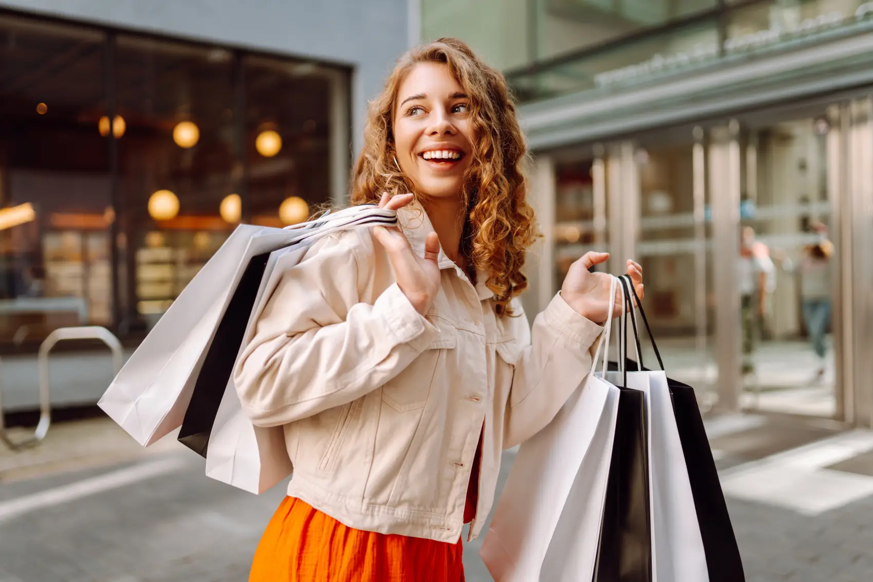 black friday 2025 - mulher loira de cabelos cacheados anda em frente a prédio com sacolas de compra na mão
