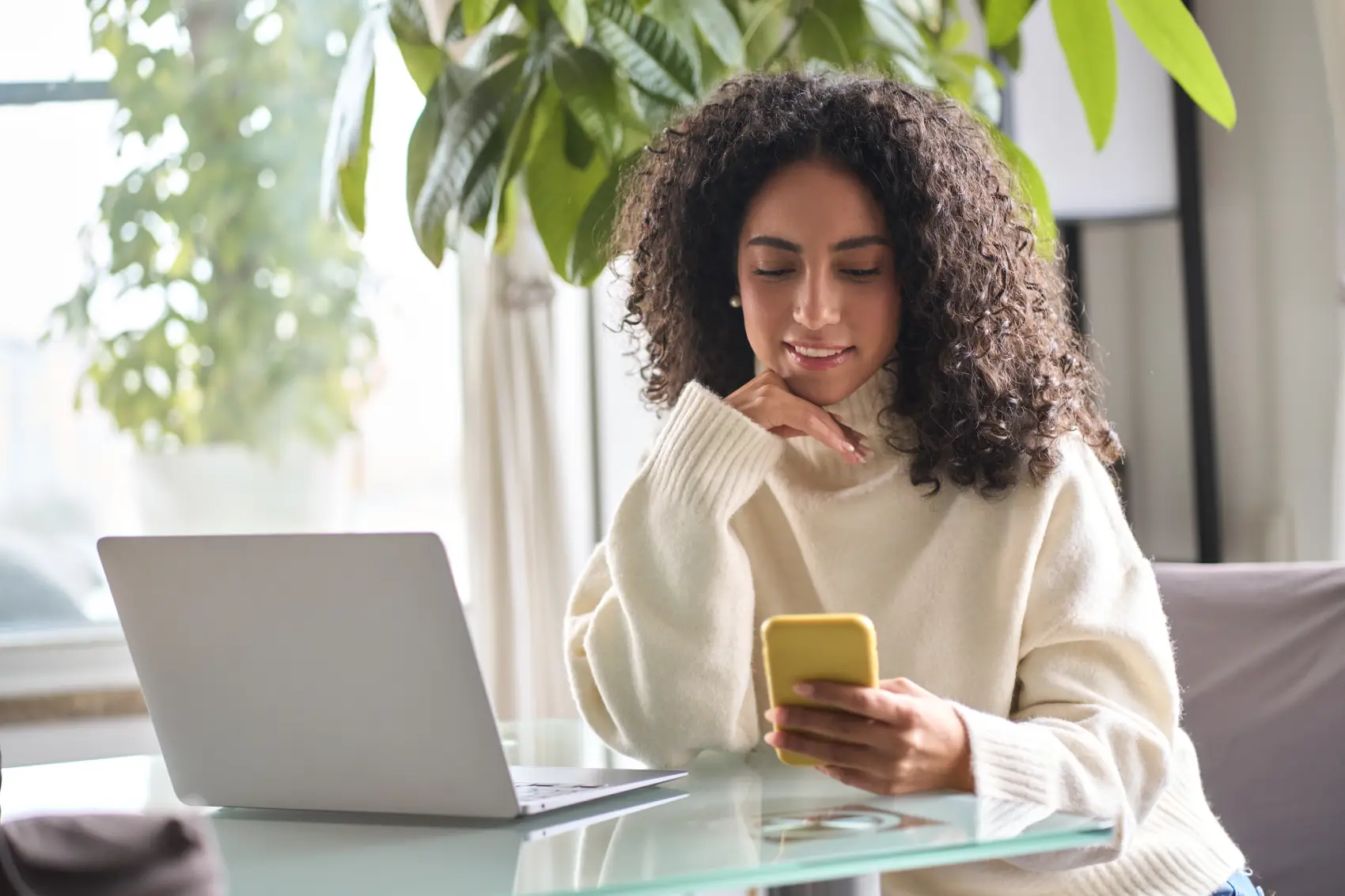 empréstimo para quitar dívidas - mulher negra feliz e pensativa em frente ao celular