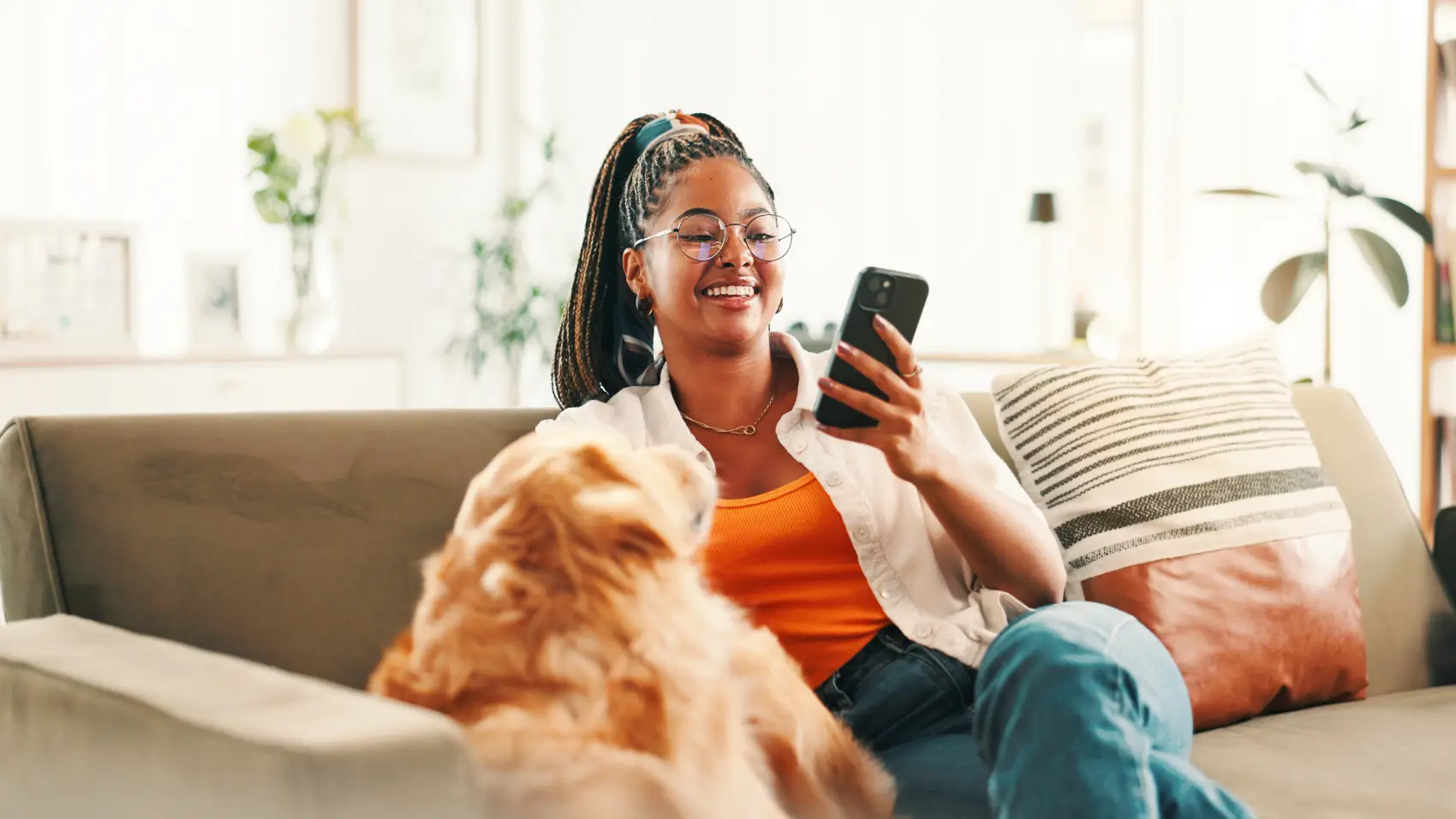 tipos de empréstimo - mulher negra sorri em frente ao celular, sentada no sofá com seu cachorro