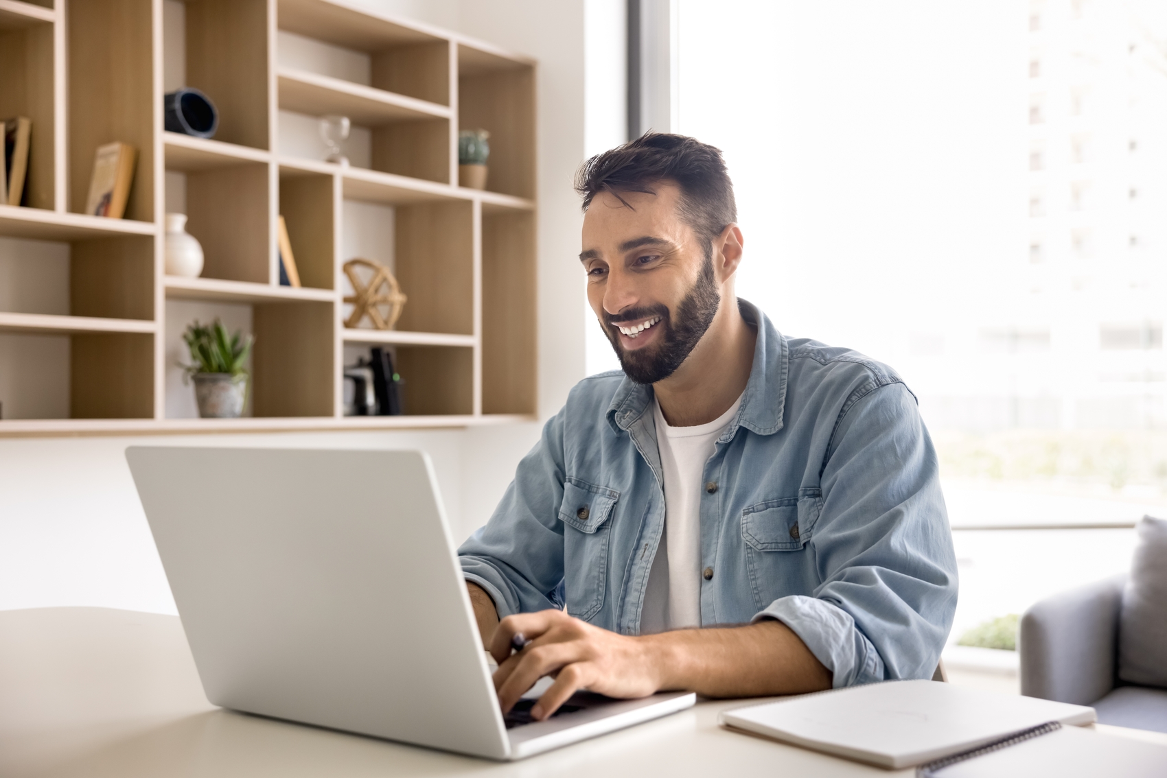 planilha de gastos​ - Jovem sorridente homem de negócios anotando informações úteis sentado na mesa com computador moderno