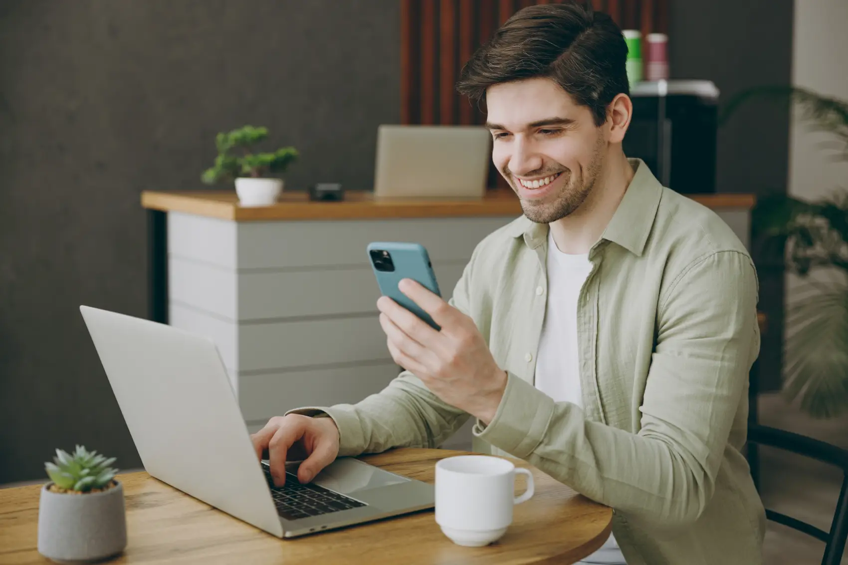 mudanças no fgts​ - homem sentado em frente ao notebook, olhando para o celular em sua mão e sorrindo
