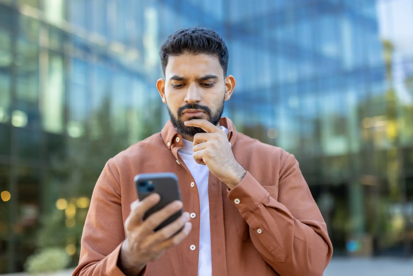 antecipação saque aniversário​ - homem pensativo olhando celular em frente a um prédio espelhado