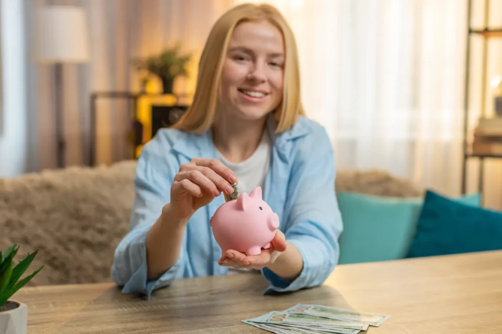 educacao-financeira-para-jovens Jovem armazena dinheiro em casa, entregando contas no mealheiro com sorriso contente e pensamento esperançoso.
