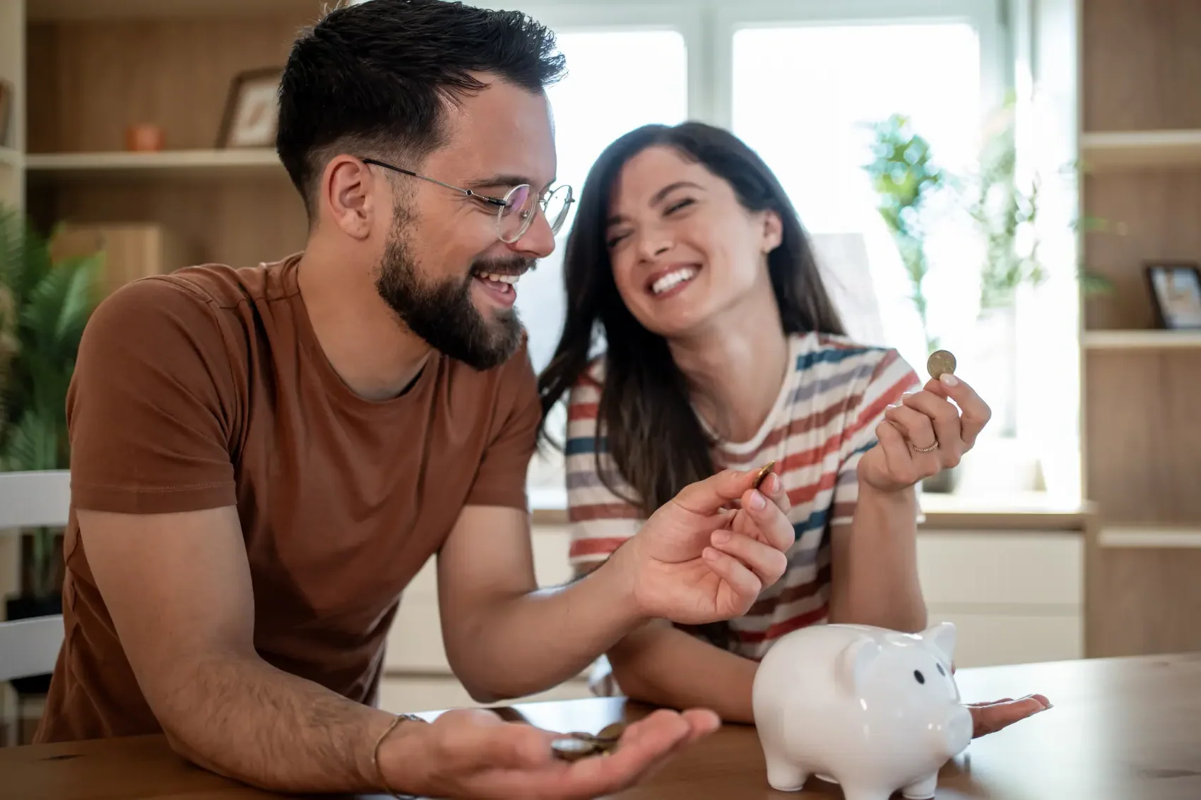 desafio 52 semanas - Jovem casal sorridente colocando moedas no cofrinho, economizando dinheiro para o futuro.