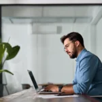 imposto de renda retido na fonte - homem de negócios latino digitando em laptop trabalhando online sentado no escritório