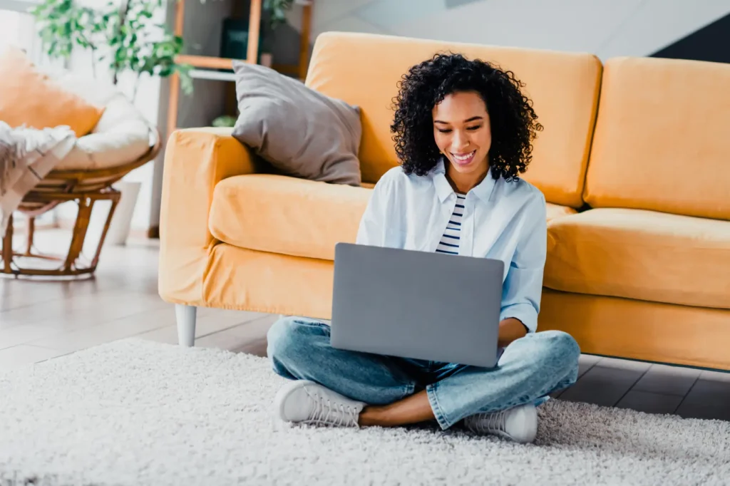 quem tem direito a isenção de imposto de renda - Jovem mulher usando um laptop enquanto senta no chão em uma sala de estar
