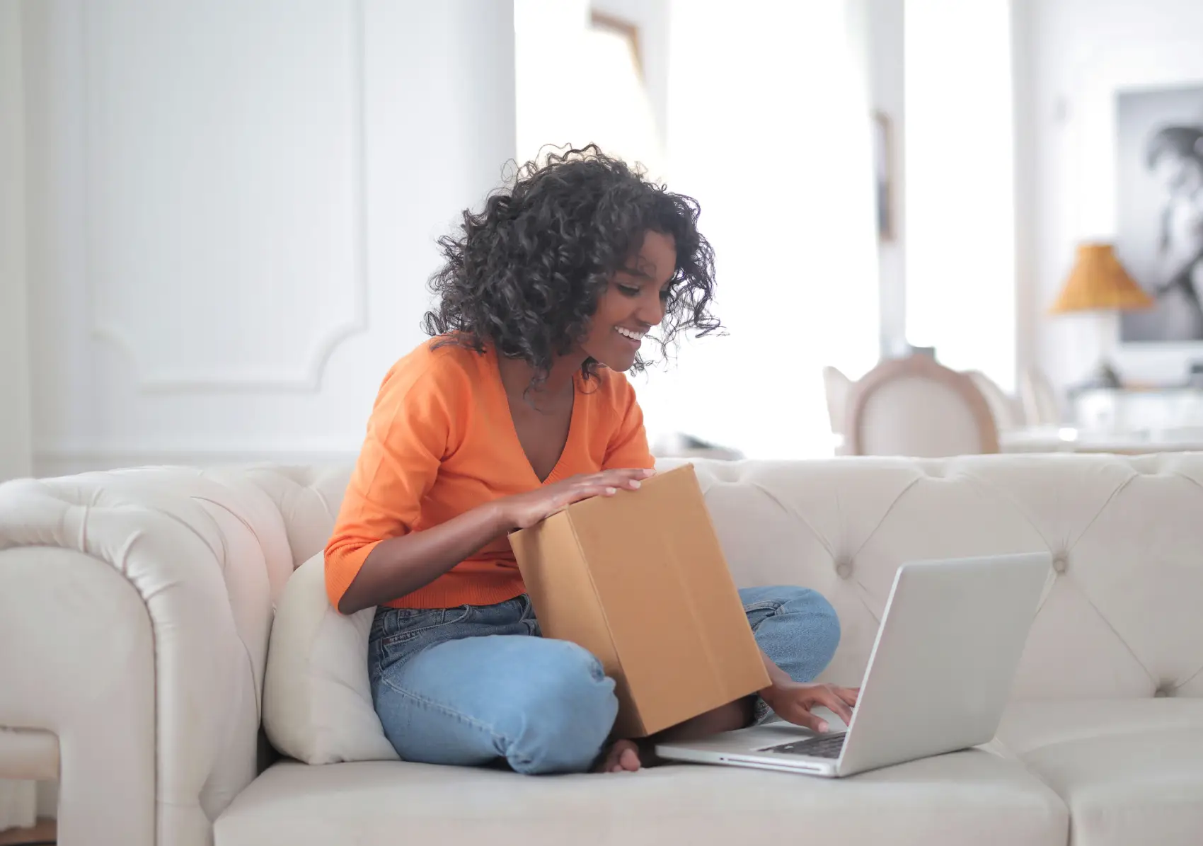 como-rastrear-encomenda-pelo-correio mulher sentada no sofá com caixa na mão e olhando para o notebook
