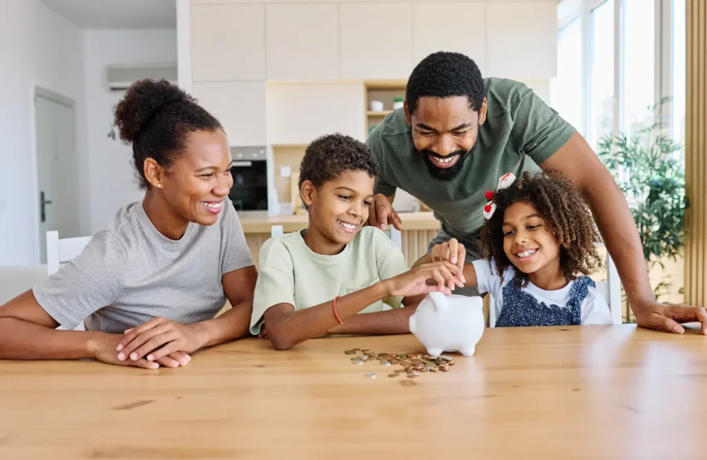 quanto-rende-1000-no-pagbank. Família de quatro mãe, pai, filha e filho colocando moeda em piggybank em casa. Conceito de poupança pessoal, segurança bancária e investimentos financeiros