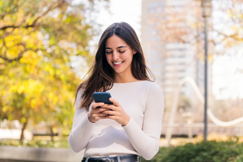 conta rendeira - Mulher caucasiana sorrindo feliz enquanto usa seu celular