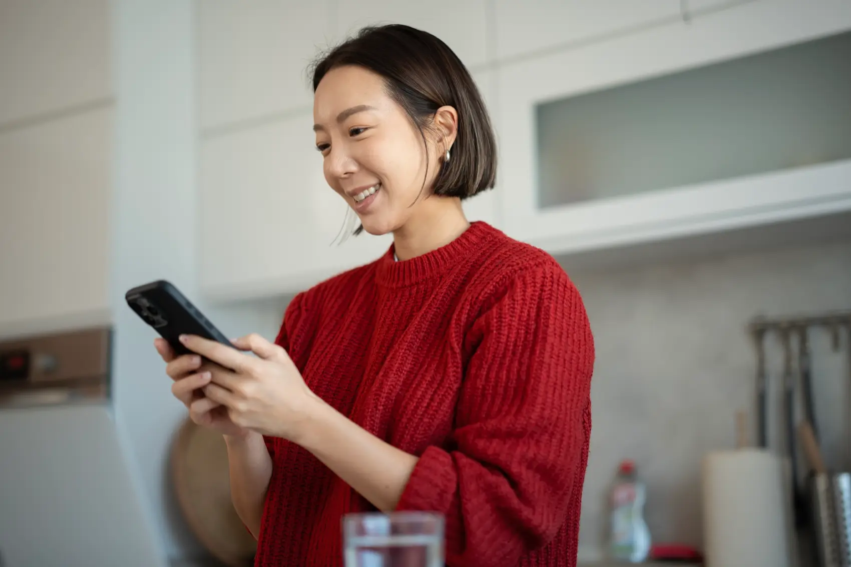 Como fazer saque do FGTS - Jovem mulher asiática sorrindo enquanto usa confortavelmente seu smartphone