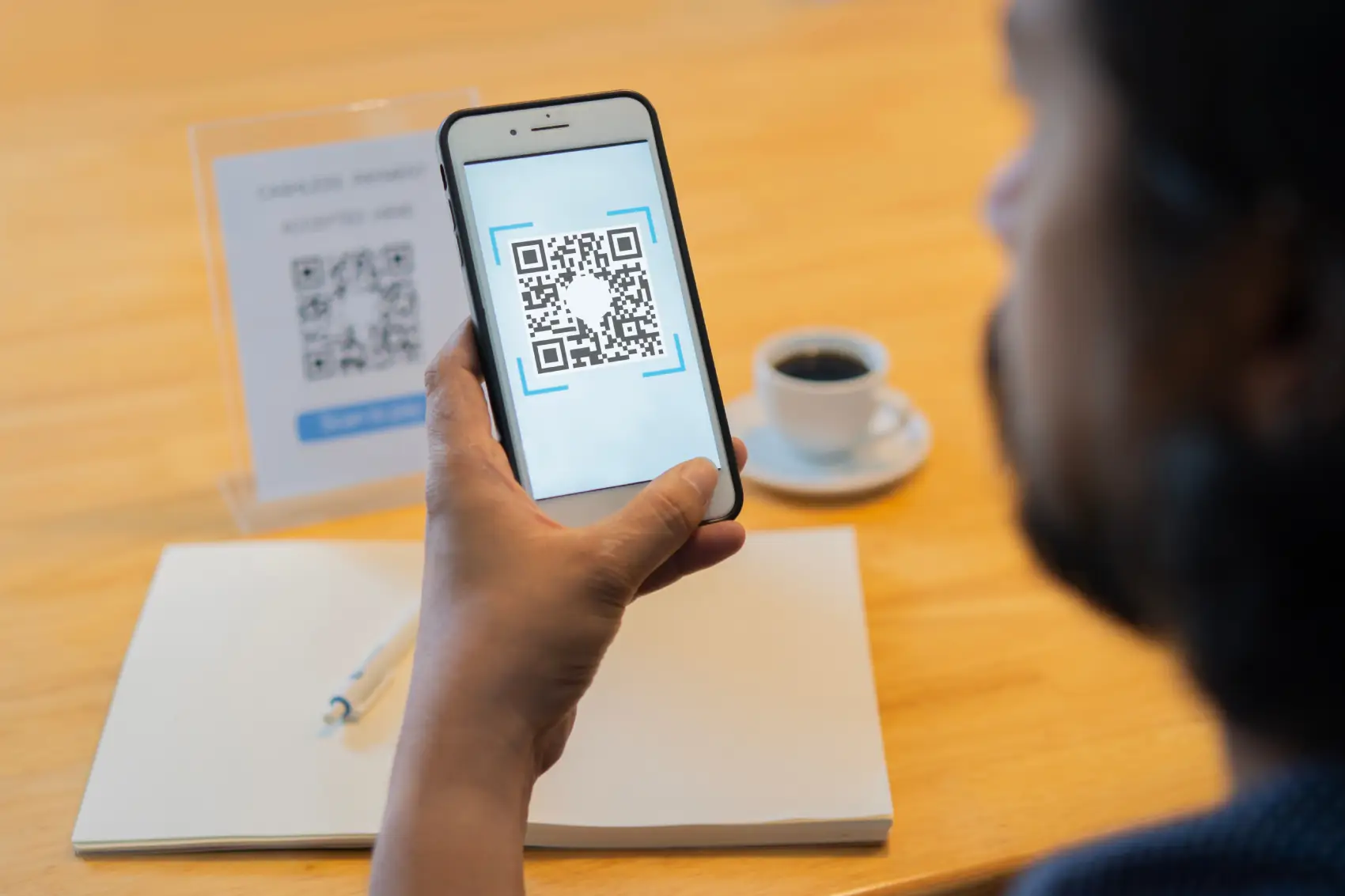 como vender com qr code​ - homem indiano escaneando qr code com celular em mesa com café