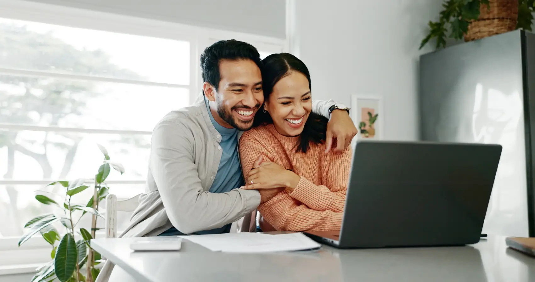 finanças para casais: casal preto abraçado e sorrindo em frente ao notebook