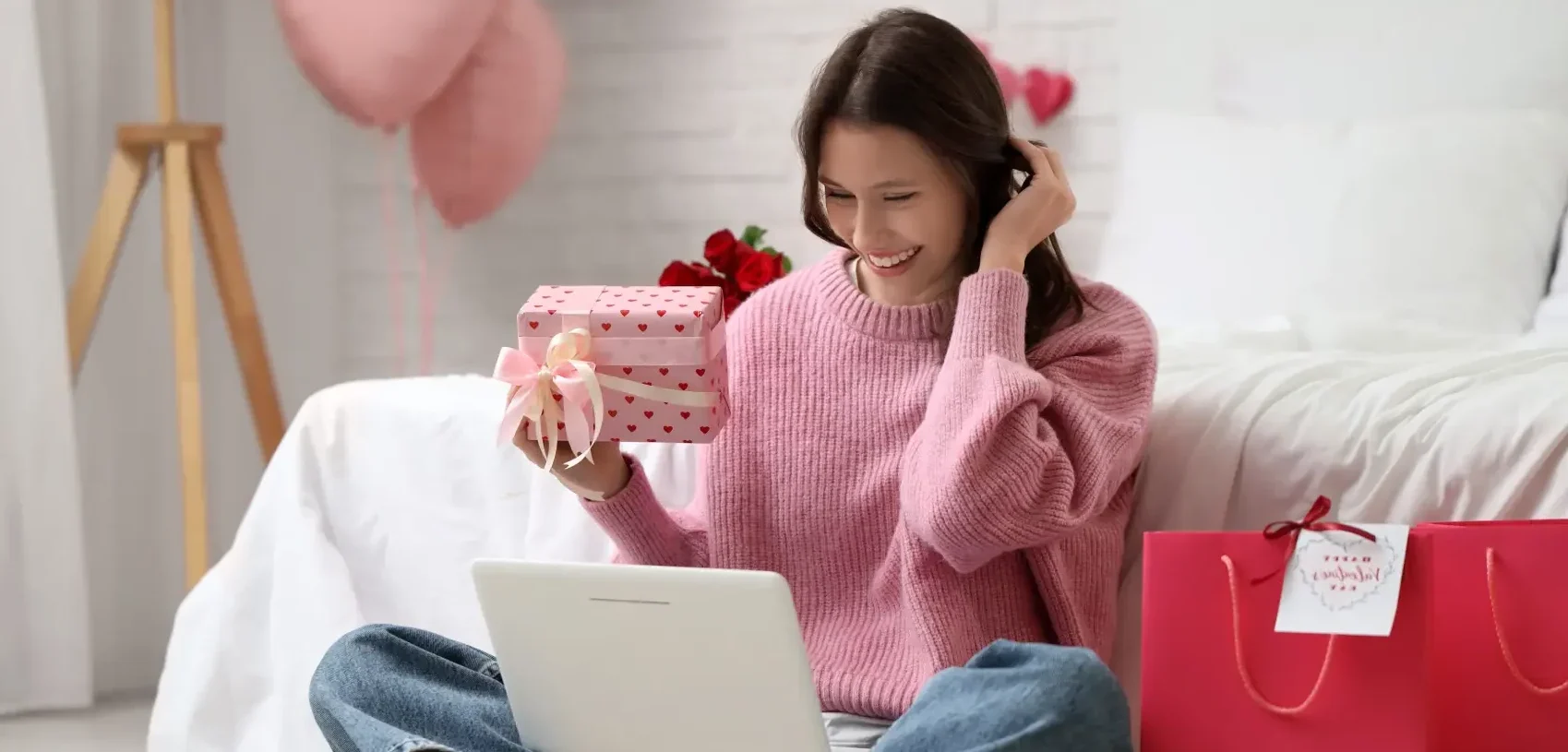 ideias para vender no dia dos namorados - Jovem mulher com laptop, presentes e sacos de compras vídeo conversando no quarto. Celebração do Dia dos Namorados