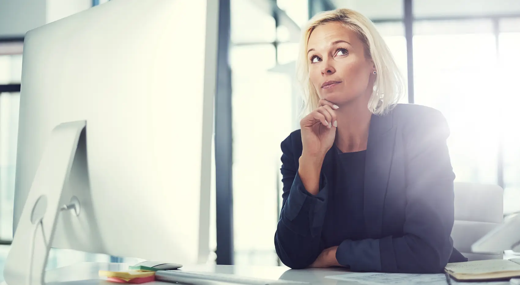 diferença entre empréstimo e financiamento​ - mulher caucasiana sentada em mesa corporativa, pensando com a mão no queixo