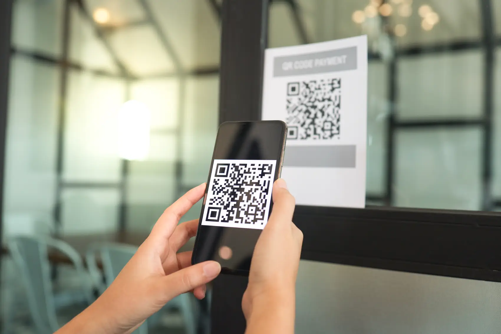 quishing​ - mão branca escaneando QR Code, que está em um vidro, com o celular