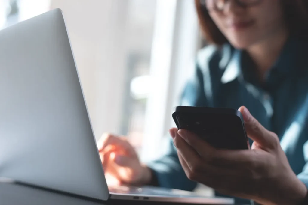 black fraude​ - pessoa sentada em mesa, em frente ao notebook e olhando o celular