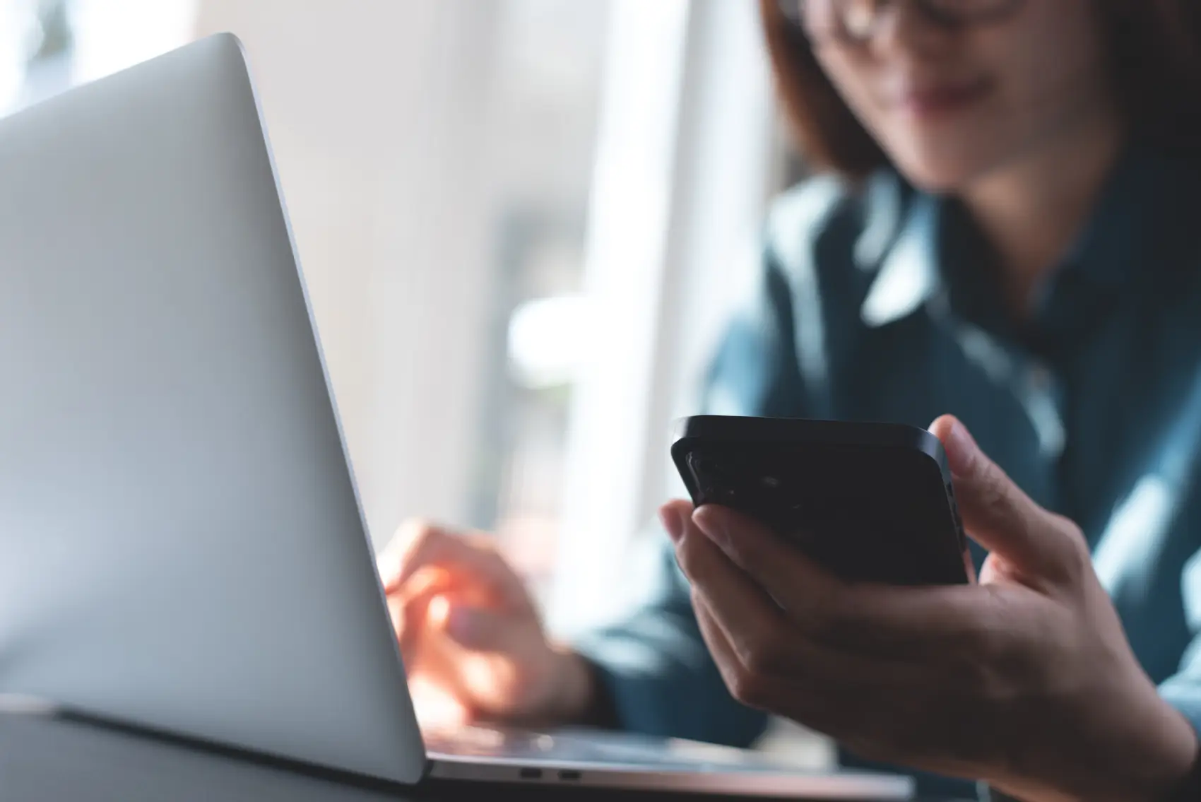 black fraude - pessoa sentada em mesa, em frente ao notebook e olhando o celular