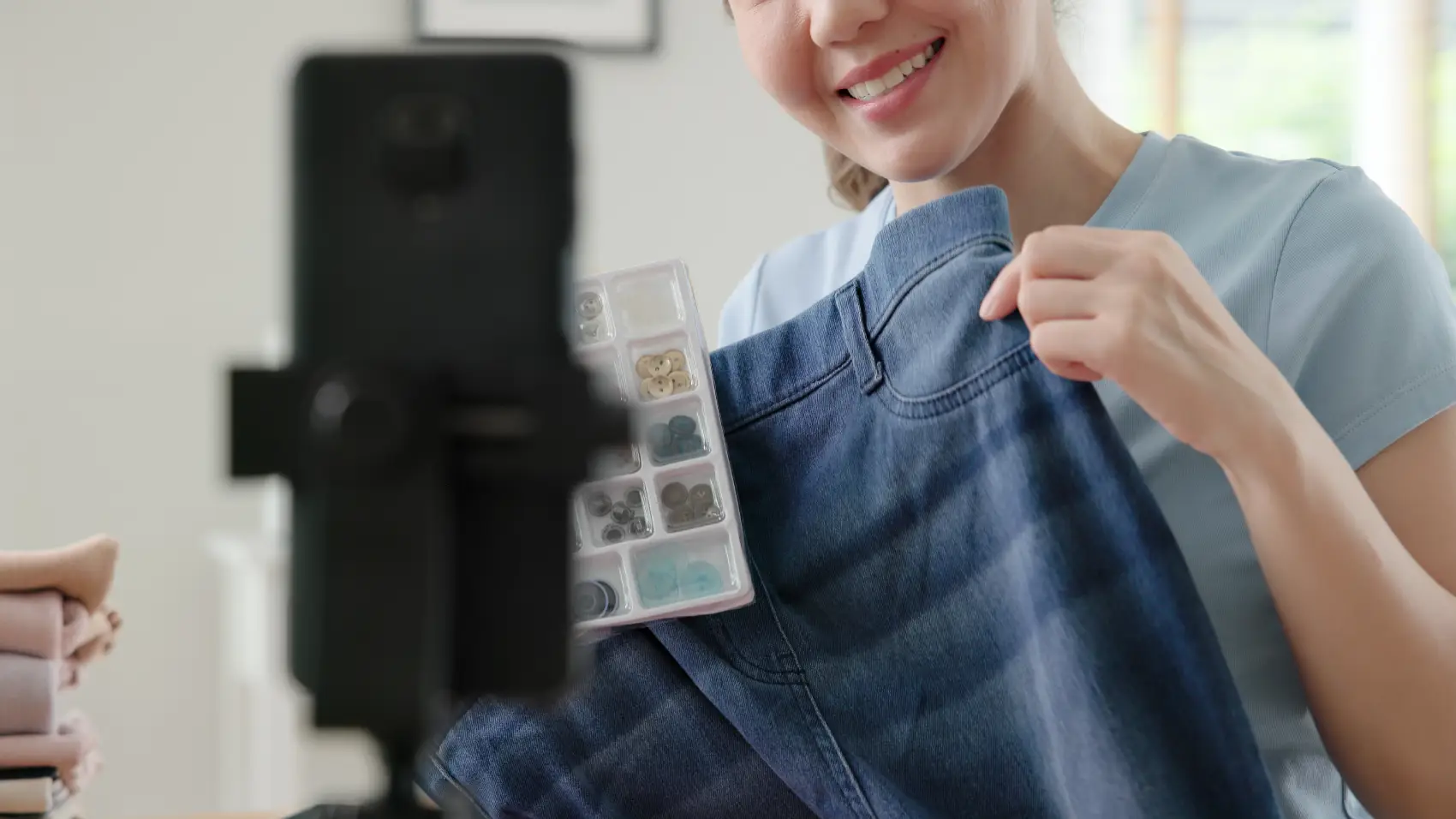 como ganhar dinheiro no instagram - mulher asiática mostrando roupa para celular, que está em apoio próprio para gravações