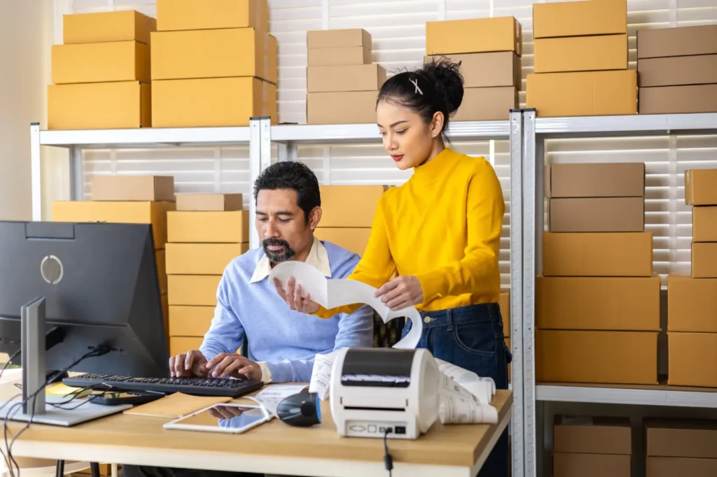 como-funciona-o-sedex casal olhando etiqueta e verificando pedidos com as caixas atrás deles.