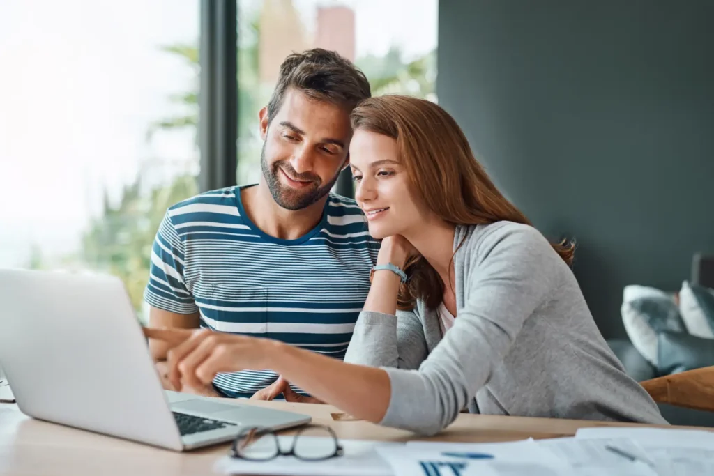 empréstimo pessoal ou consignado: homem e mulher caucasianos em frente ao notebook, sorrindo. mulher toca a tela.