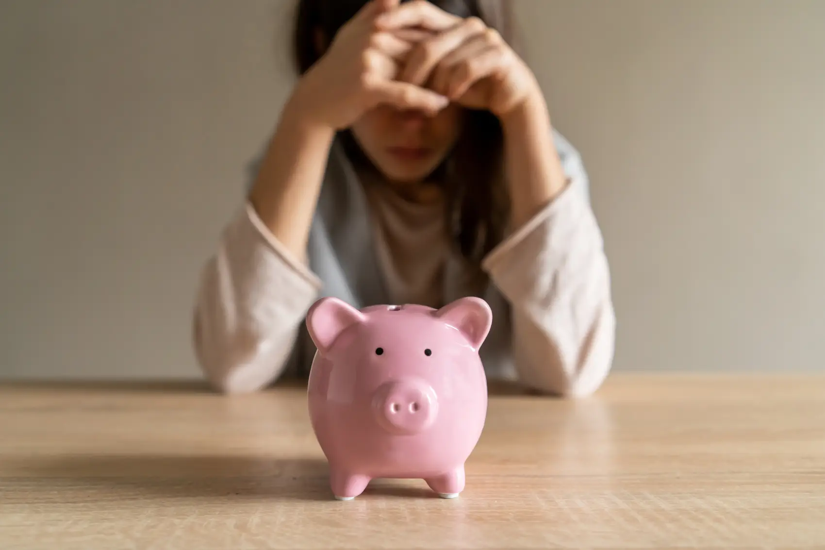 gastos invisíveis: menina triste encostada na mesa, cobrindo o rosto com as mãos; em primeiro plano, um cofrinho rosa em forma de porquinho.