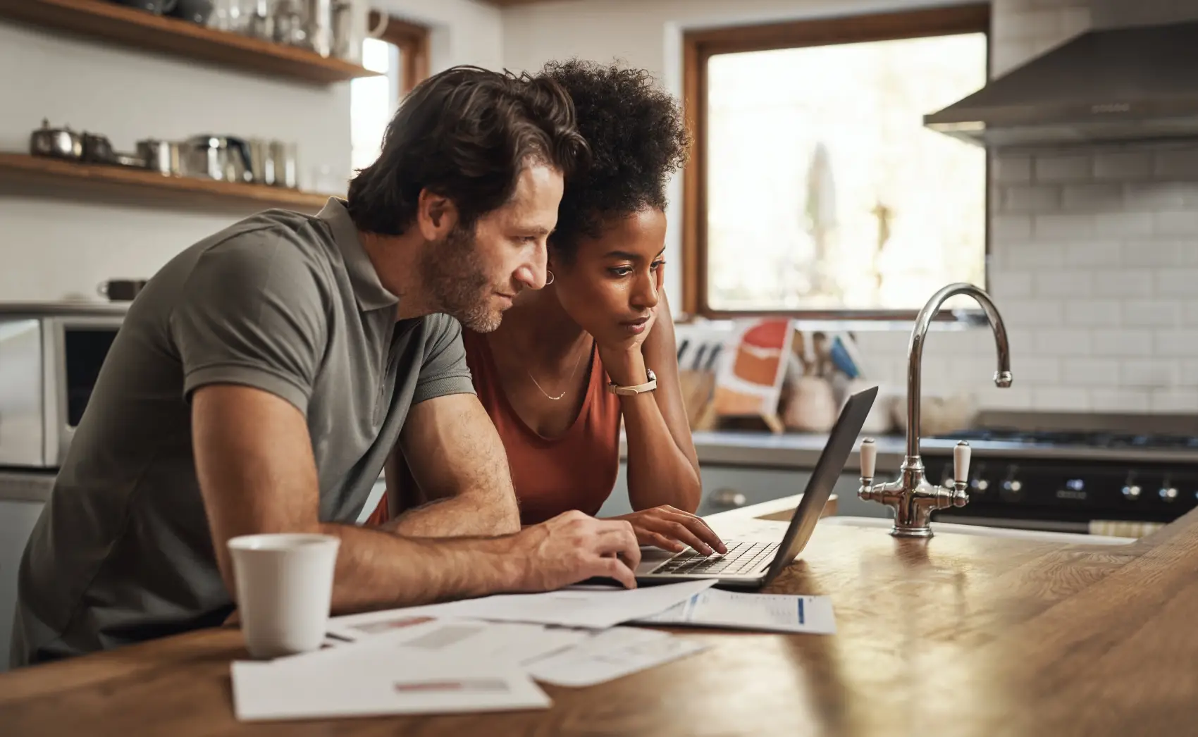o que é custo efetivo total​ - Casal interracial fazendo planejamento financeiro na cozinha, em frente ao laptop, com documentos para orçamento, poupança e pagamento de contas