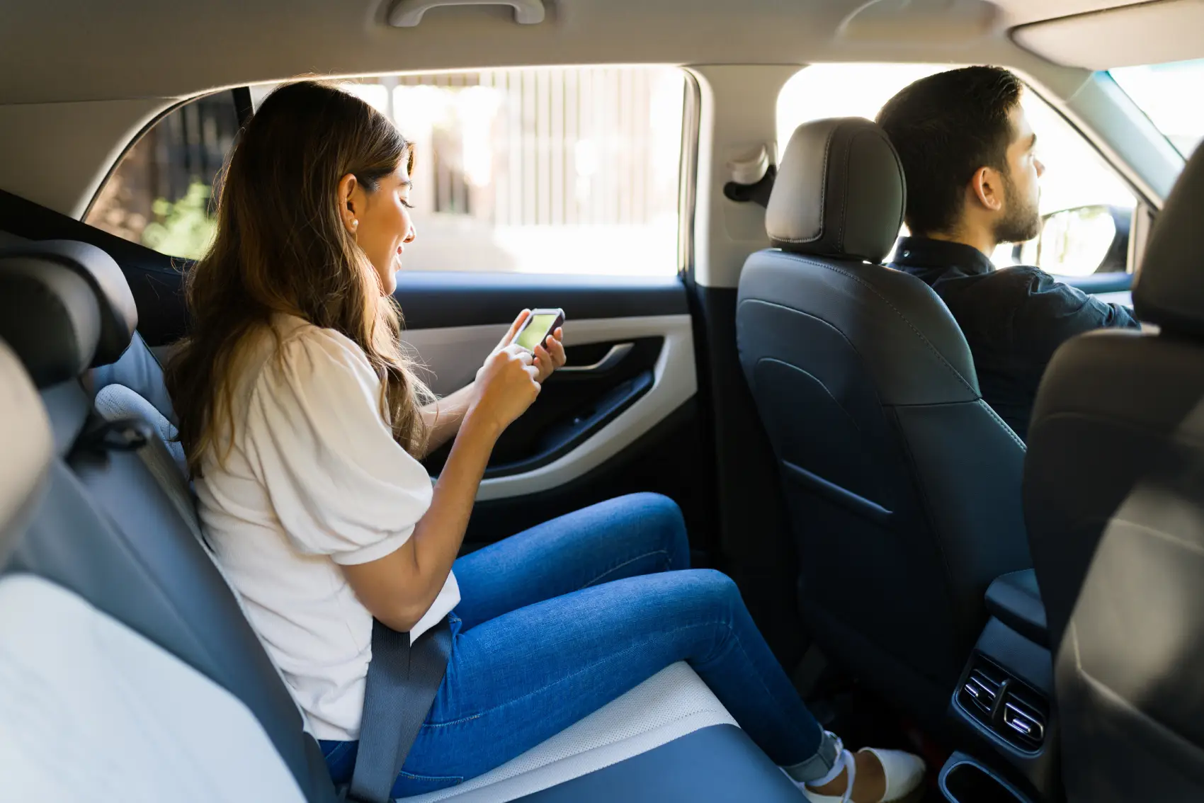 como ser motorista de aplicativo - Vista lateral de uma mulher latina atraente sentada no banco de trás de um carro, usando um aplicativo de transporte por aplicativo em seu smartphone