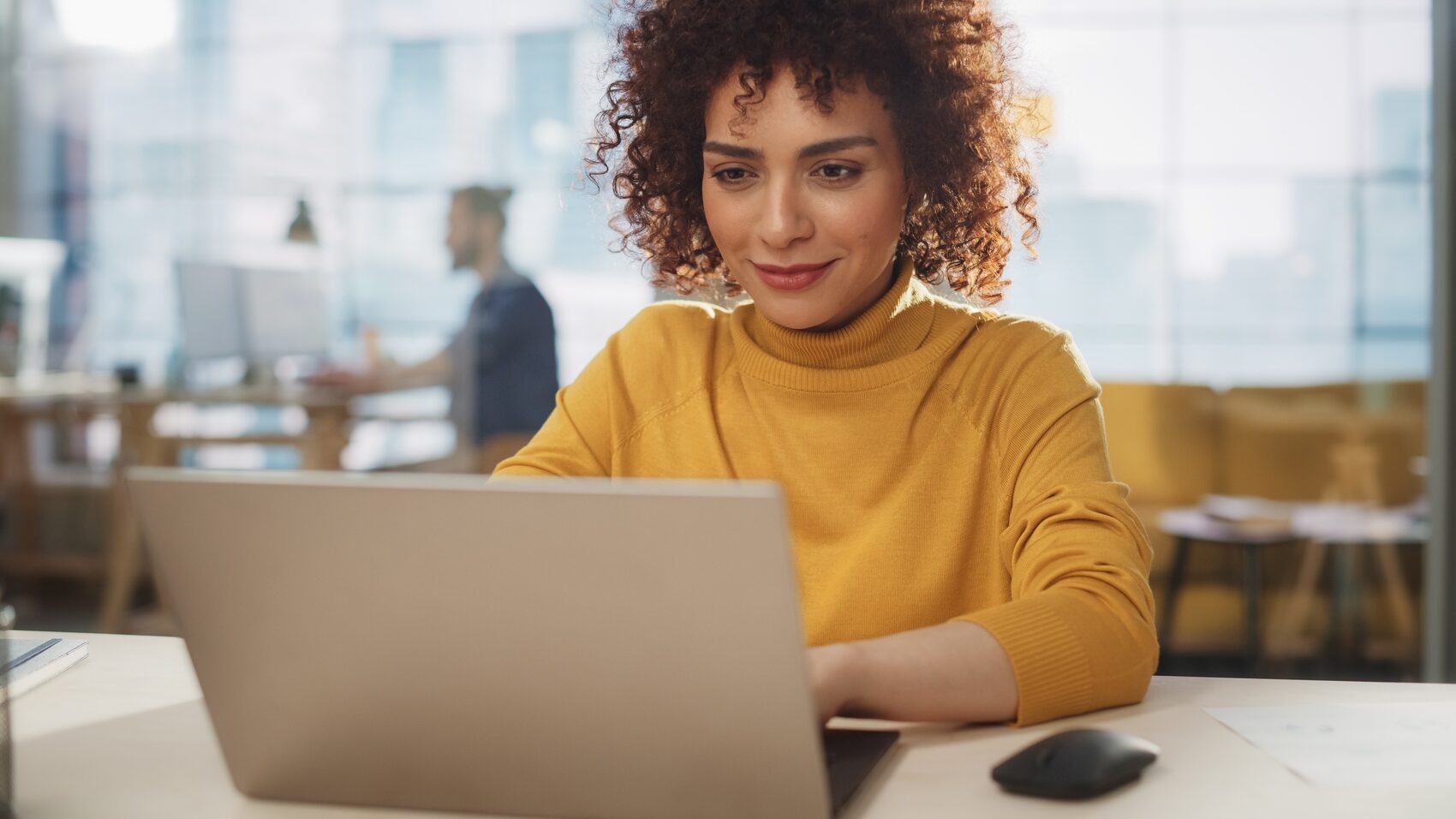 ia para marketing - Jovem elegante de cabelos cacheados usando um computador portátil em uma agência de marketing.