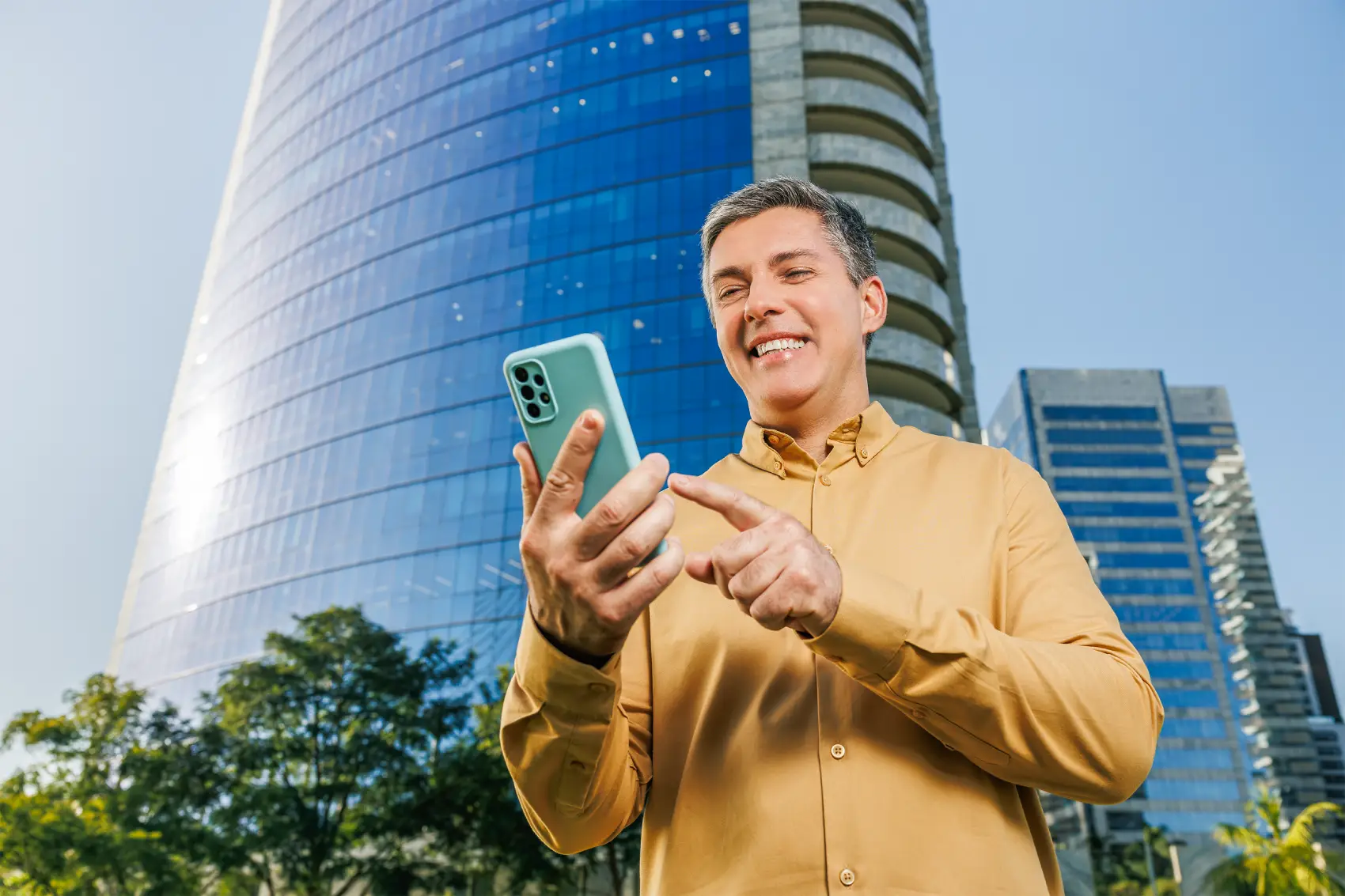 seguros pagbank - homem grisalho usando celular na rua em frente a um prédio espelhado