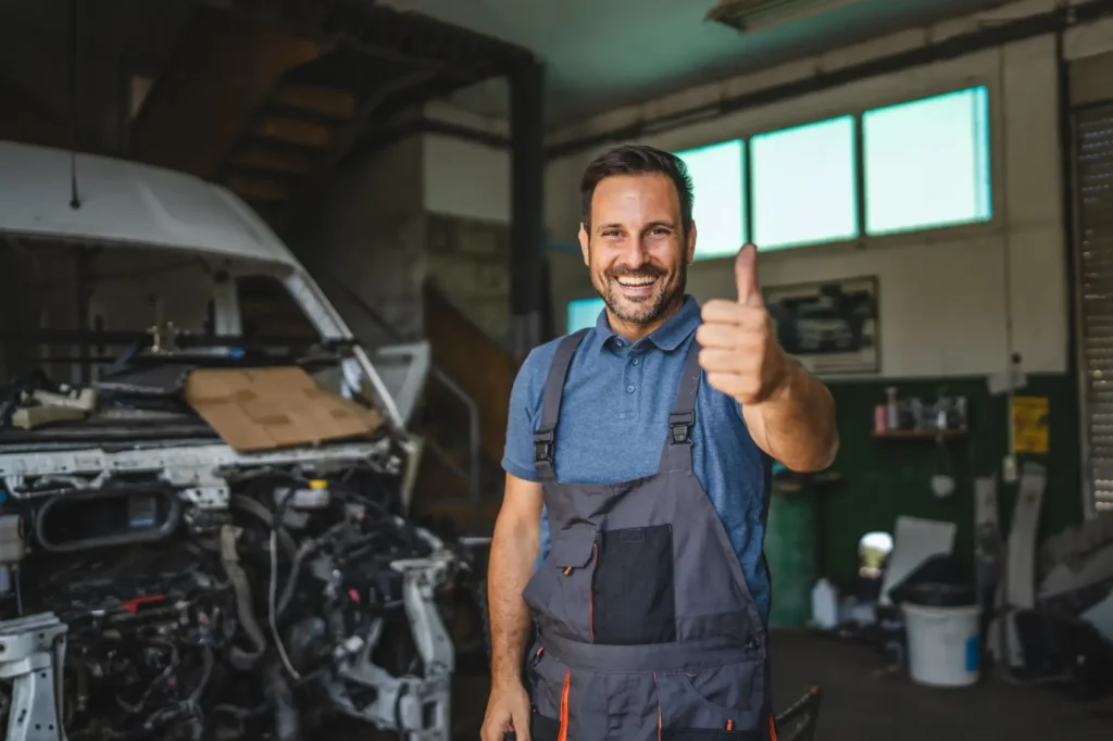 como abrir uma oficina mecanica - Um mecânico alegre de macacão sorri com confiança, dando um polegar para cima em uma oficina, transmitindo satisfação e prontidão para ajudar com qualquer reparação de carro.