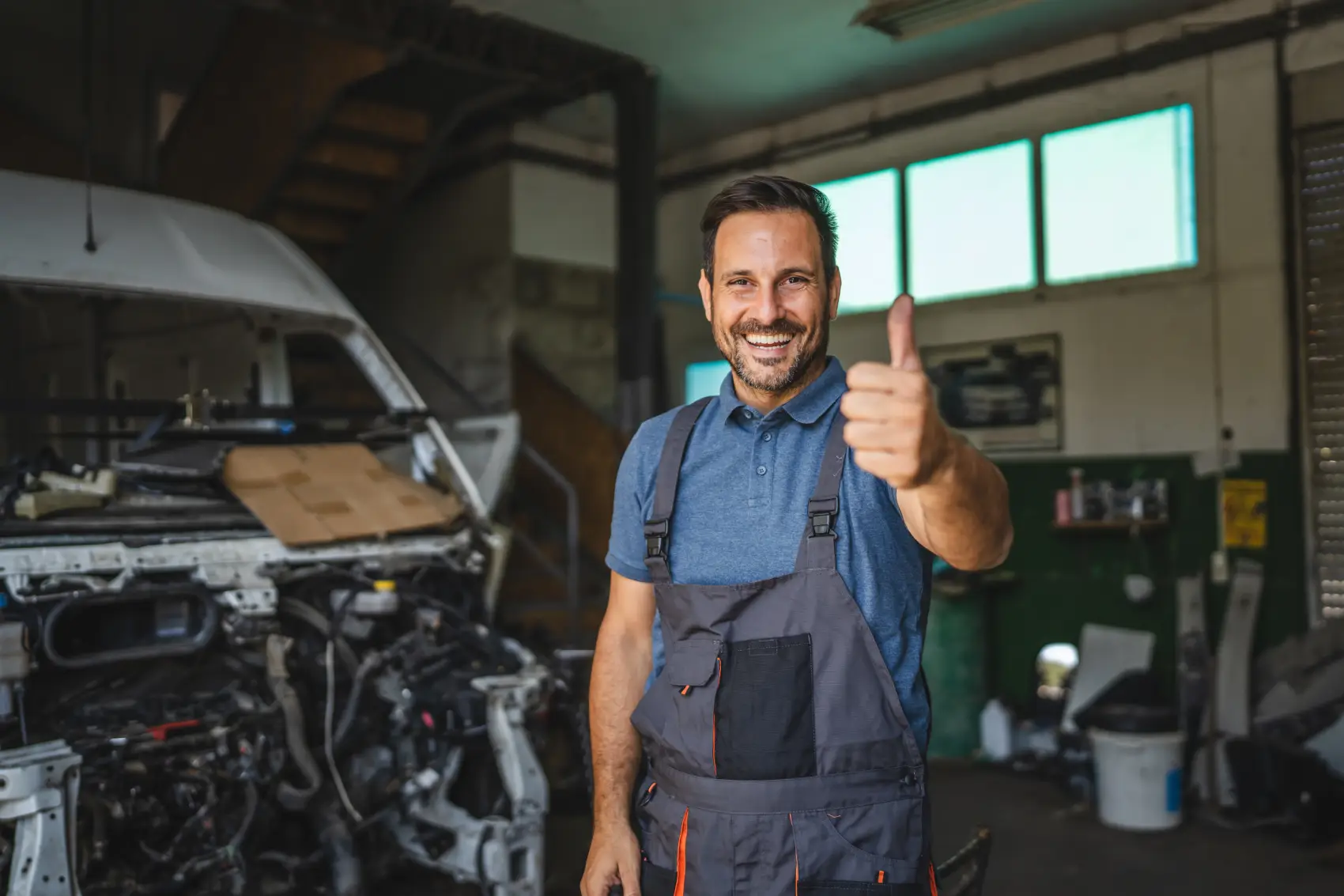 como abrir uma oficina mecanica - Um mecânico alegre de macacão sorri com confiança, dando um polegar para cima em uma oficina, transmitindo satisfação e prontidão para ajudar com qualquer reparação de carro.