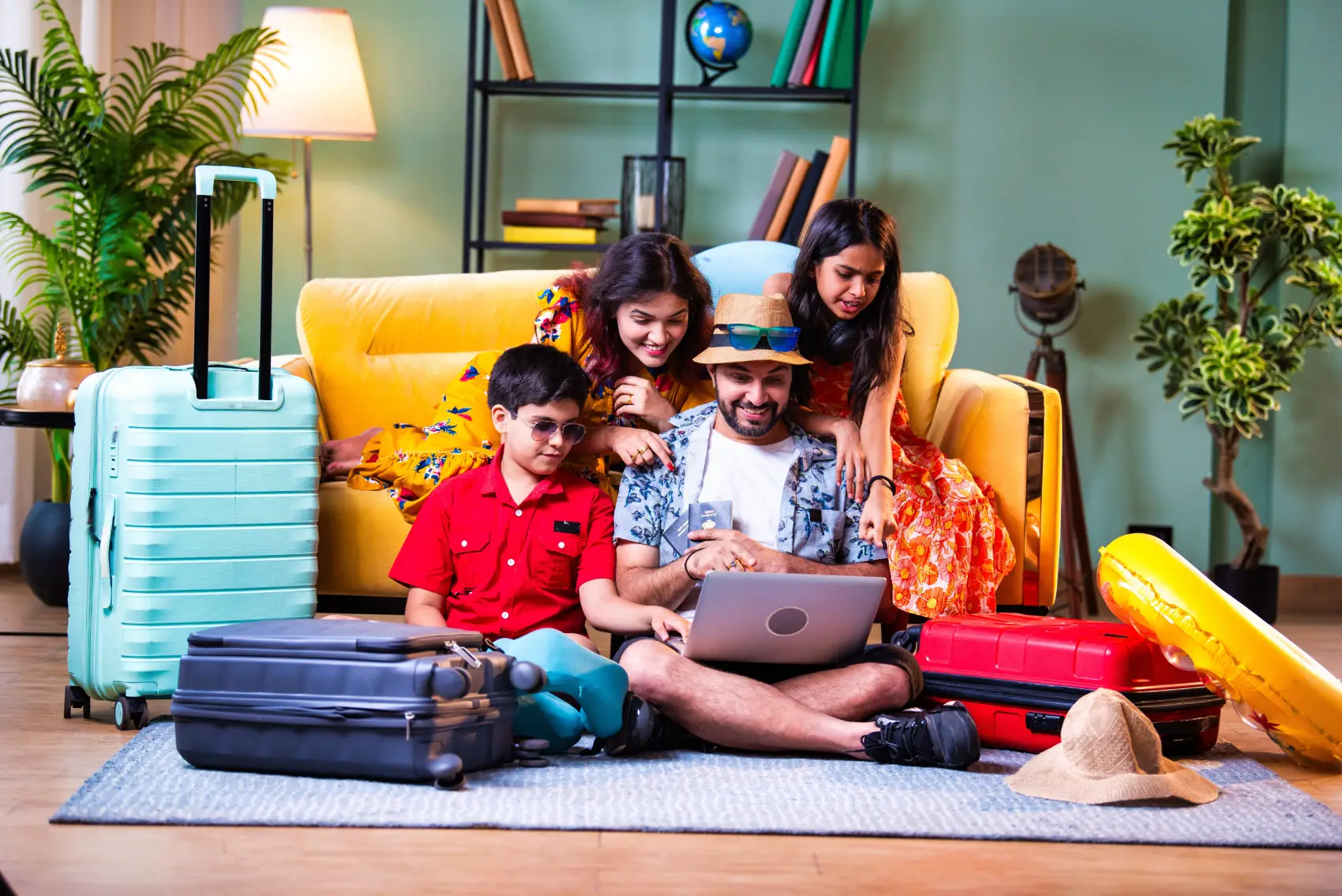 planejamento-financeiro-familiar Família feliz de quatro com laptop e malas em casa moderna fazendo web check-in ou reservando uma viagem de férias