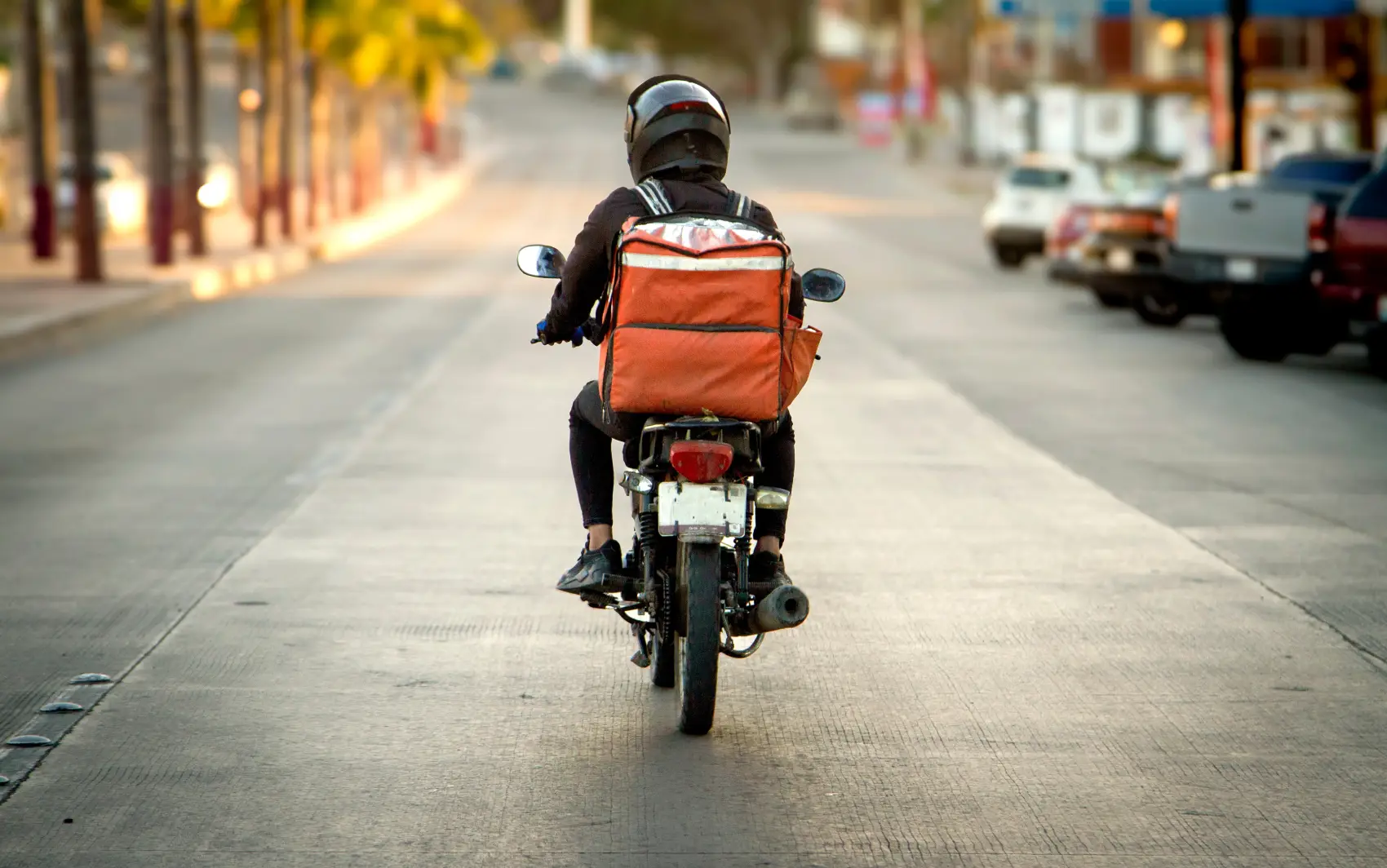 cnpj para entregador​ - Entregador de comida em uma motocicleta em uma rodovia, fotografado por trás