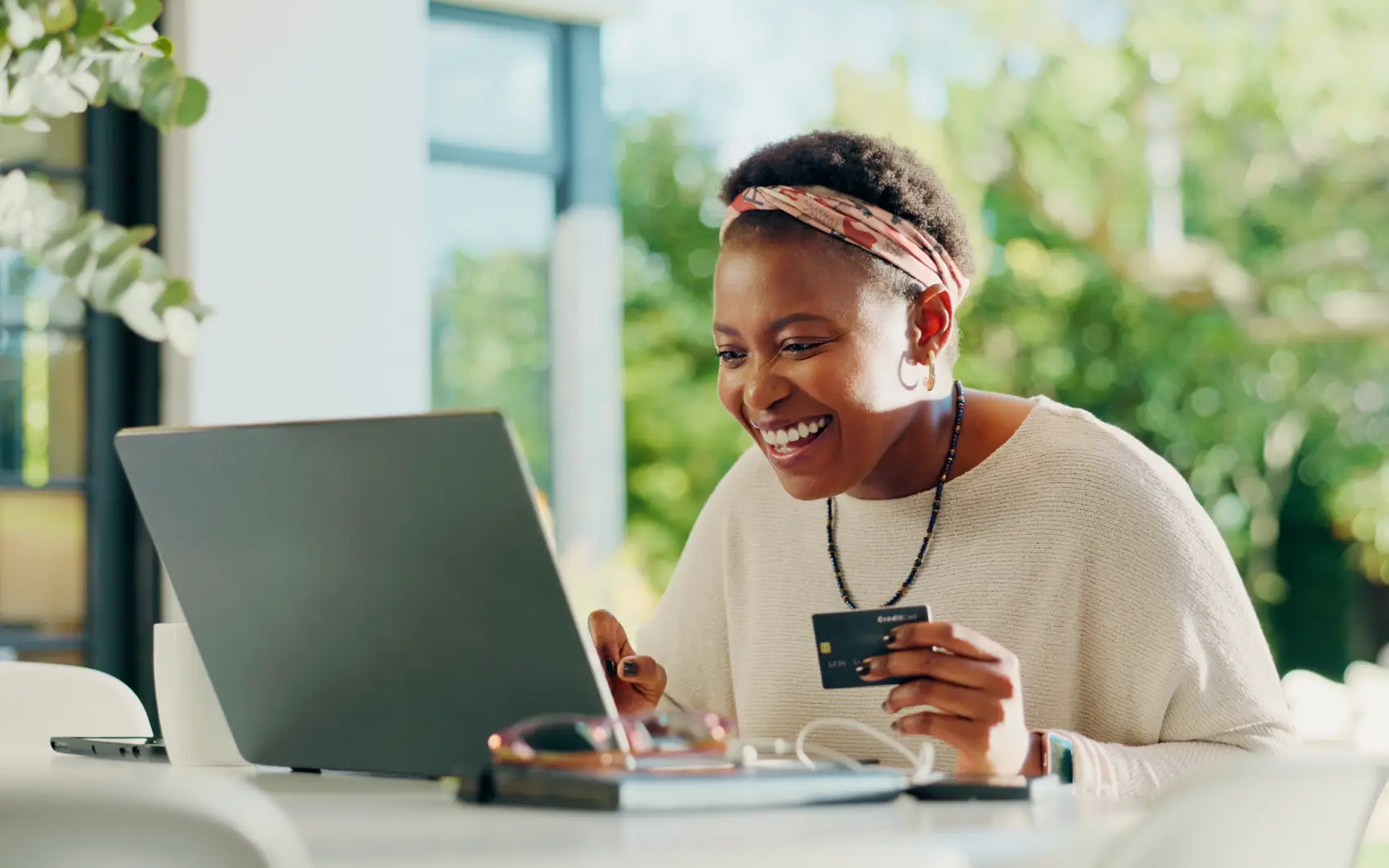 como economizar na Black Friday - mulher negra sorri em frente ao laptop com cartão de crédito em mãos