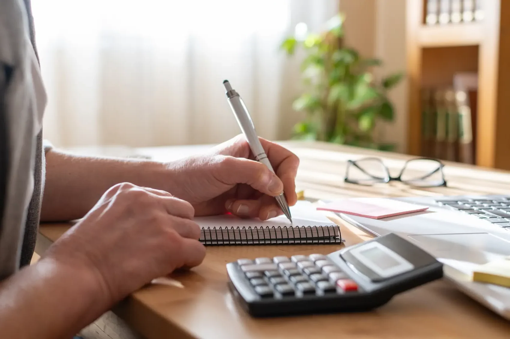 como investir em previdência privada - Mãos da pessoa usando uma calculadora e escrevendo notas em um caderno, gerenciando finanças, planejando orçamento e trabalhando em soluções para operações de negócios em uma mesa