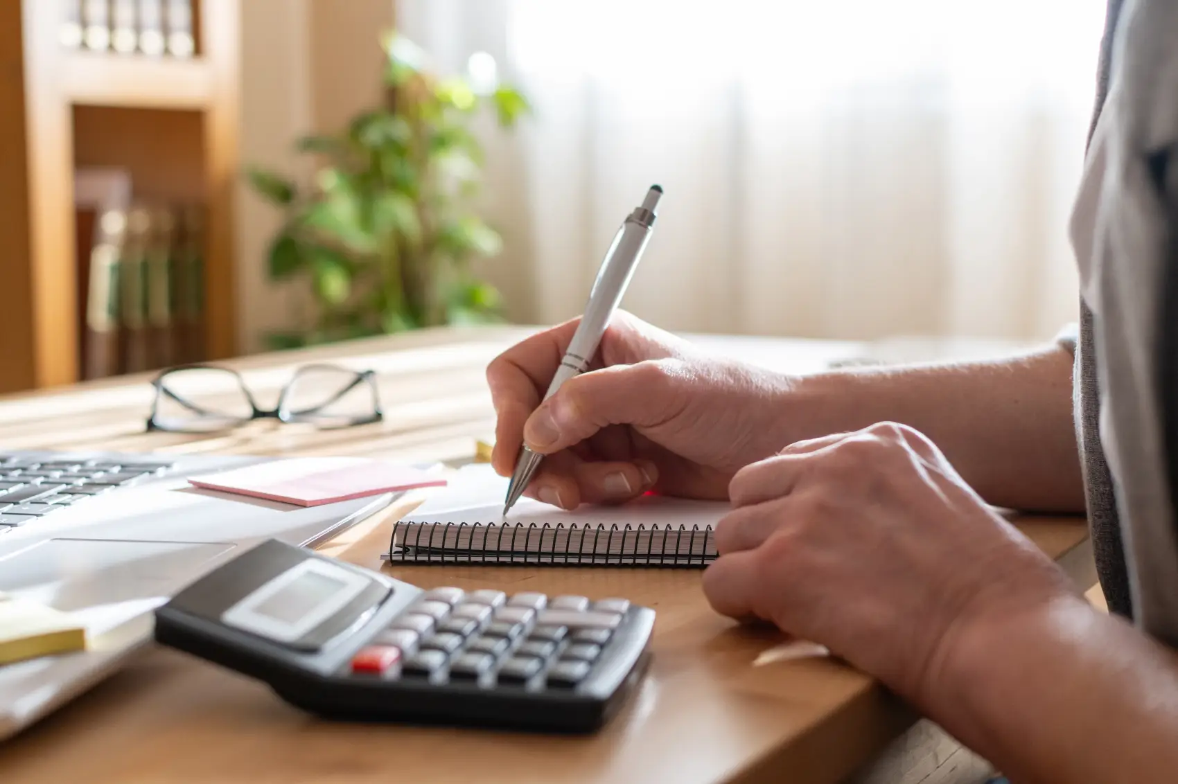 como investir em previdência privada - Mãos da pessoa usando uma calculadora e escrevendo notas em um caderno, gerenciando finanças, planejando orçamento e trabalhando em soluções para operações de negócios em uma mesa